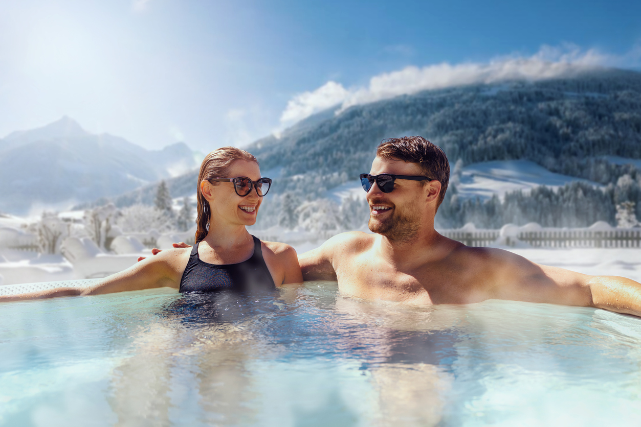 Smiling couple relaxing in an outdoor hot spring with Swiss Alps in the background, symbolizing expat benefits under the US-Switzerland Totalization Agreement to avoid double Social Security taxes.